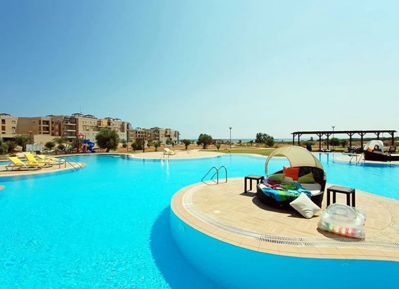 Poolside view of the luxurious Thalassa Beach Resort with clear blue waters and sun loungers.