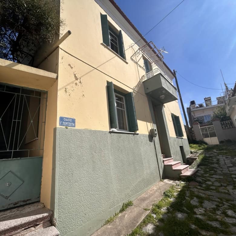 Cozy two-story house with green shutters and a small balcony in a sunny neighborhood.