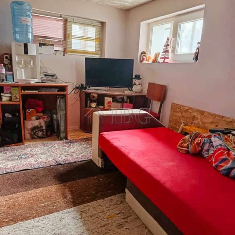 Interior of a cozy living room with a red sofa, TV, water dispenser, and natural light from windows.