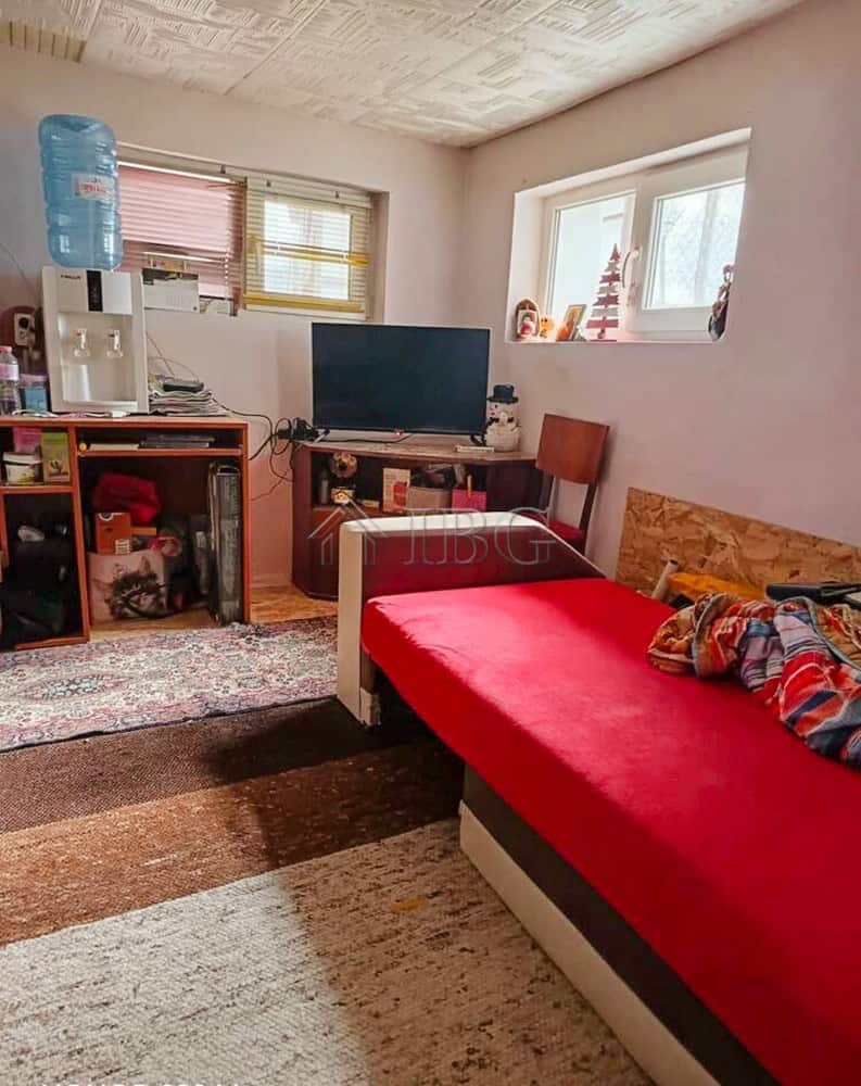 Interior of a cozy living room with a red sofa, TV, water dispenser, and natural light from windows.