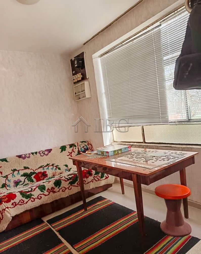Bright living space featuring a large window, floral sofa cover, and a wooden table with colorful ru.