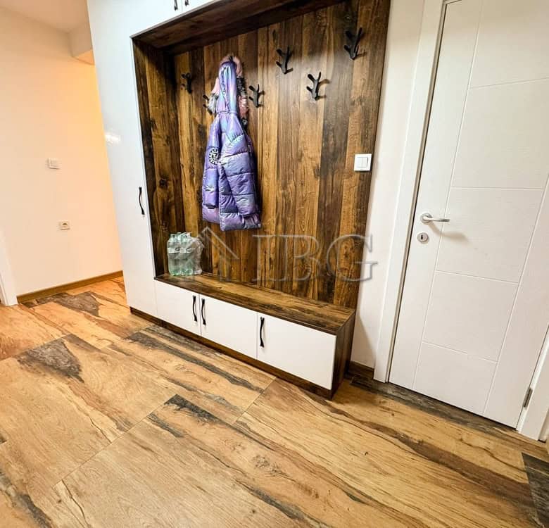 Entryway with wooden wall panel, hooks, and storage bench in a spacious apartment.