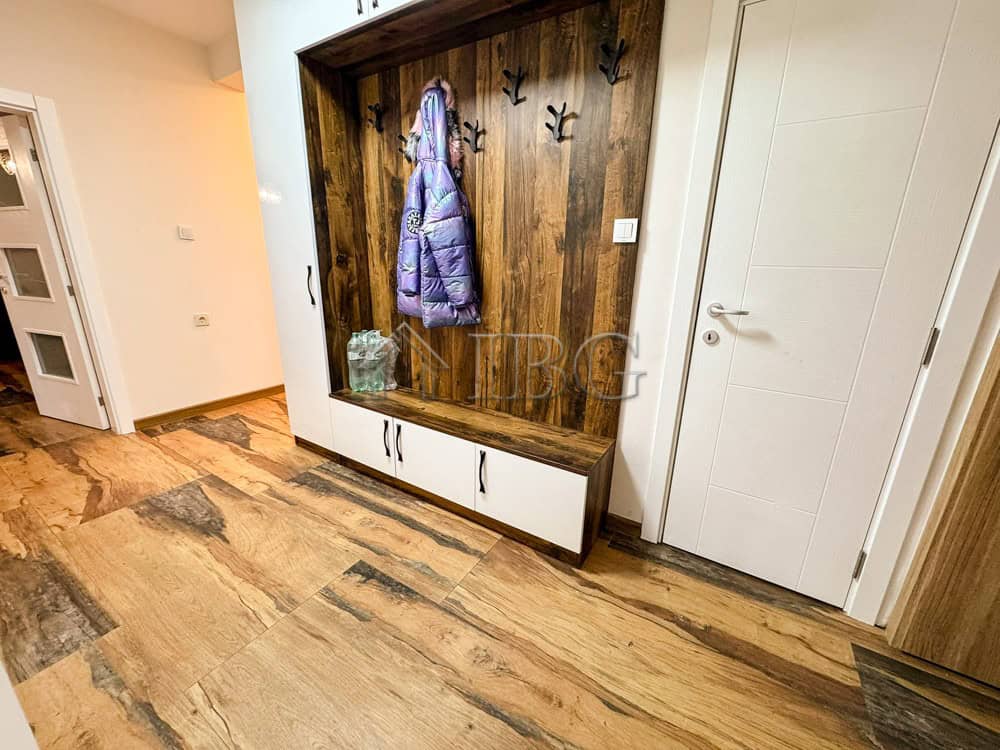 Entryway with wooden wall panel, hooks, and storage bench in a spacious apartment.