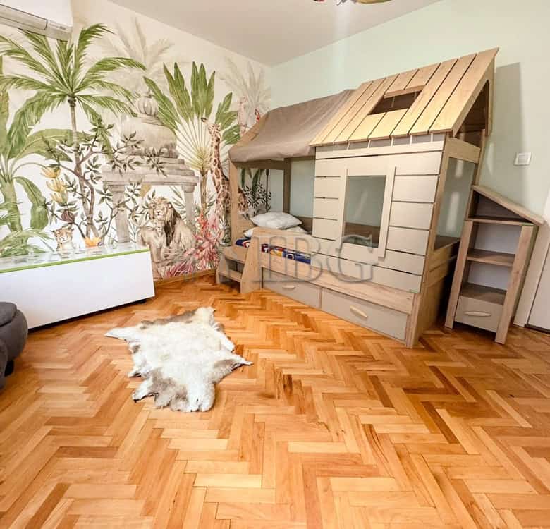 Child's bedroom with a wooden playhouse bed and jungle-themed wallpaper.