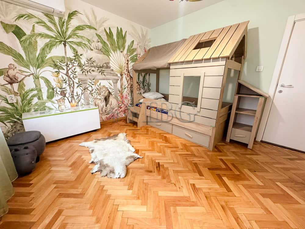 Child's bedroom with a wooden playhouse bed and jungle-themed wallpaper.
