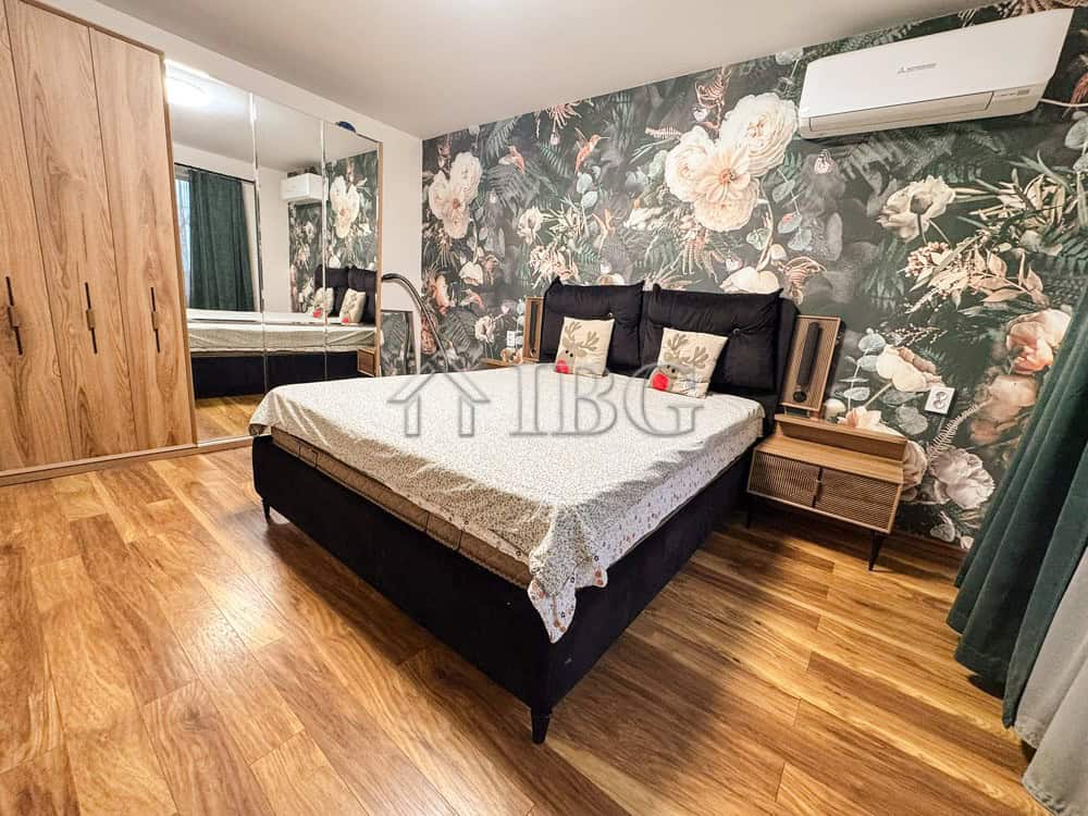 Modern bedroom with floral accent wall and wooden flooring.