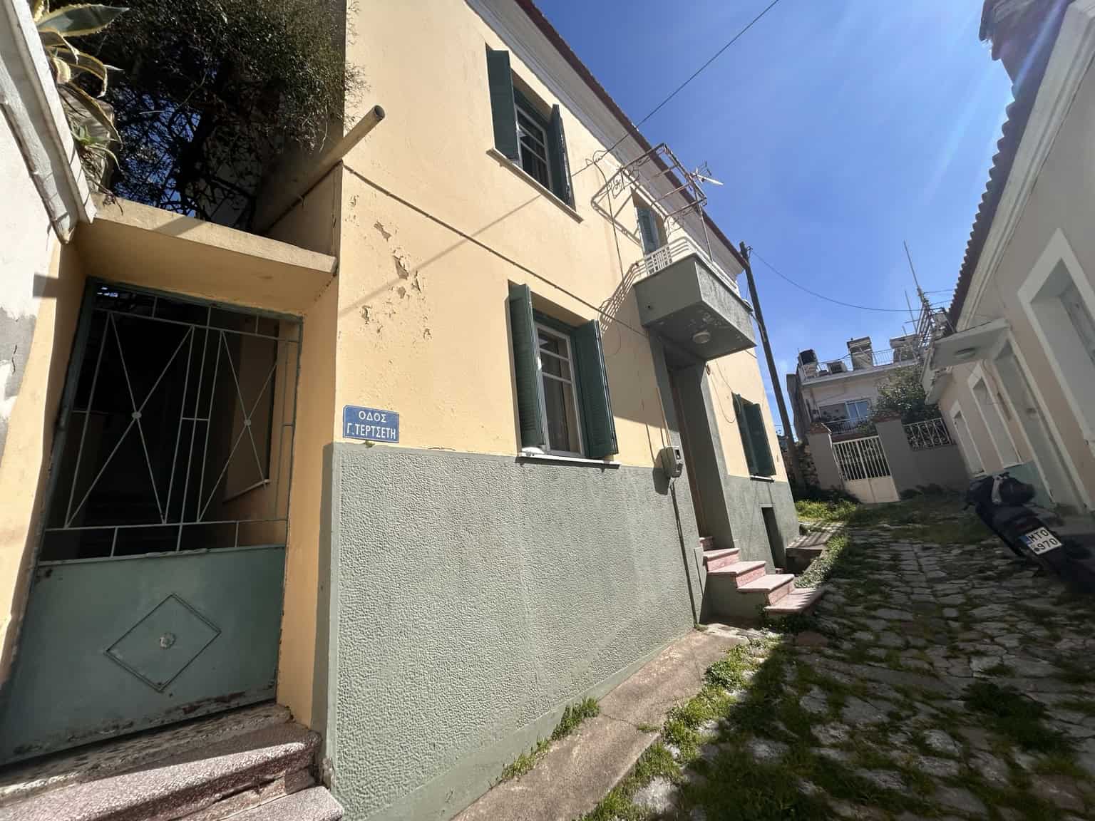 Cozy two-story house with green shutters and a small balcony in a sunny neighborhood.