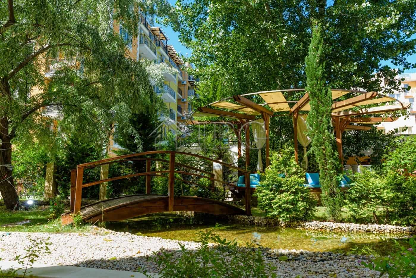 Beautiful garden scene featuring a wooden bridge, lush greenery, and a shaded seating area in Sunny.