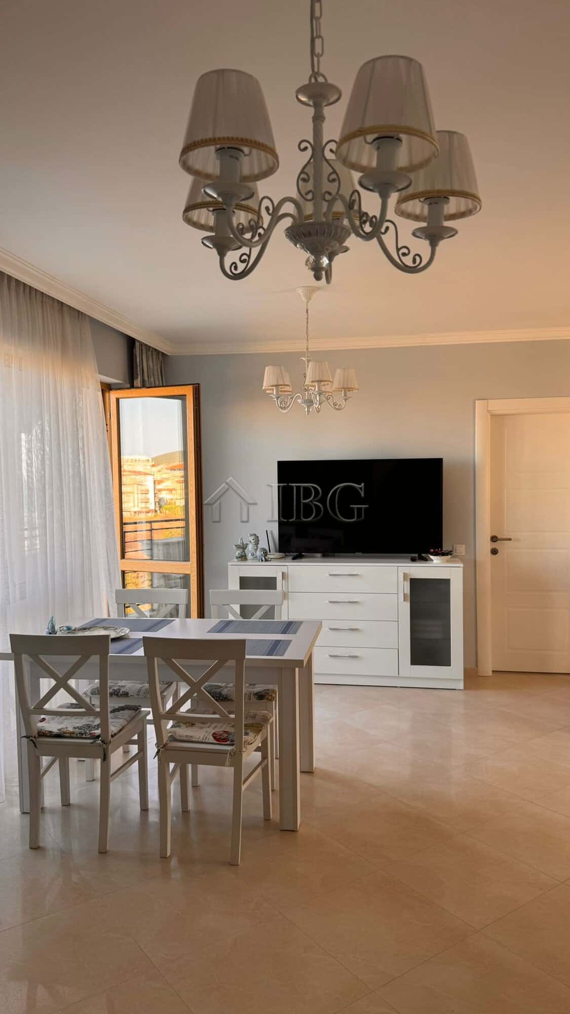 Bright living room with dining table, chandelier, and balcony view in Sveti Vlas apartment.