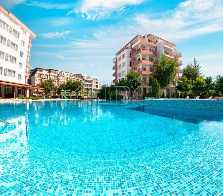 Pool with apartment buildings at Riviera Fort Beach, Ravda, featuring sea views and lush greenery.