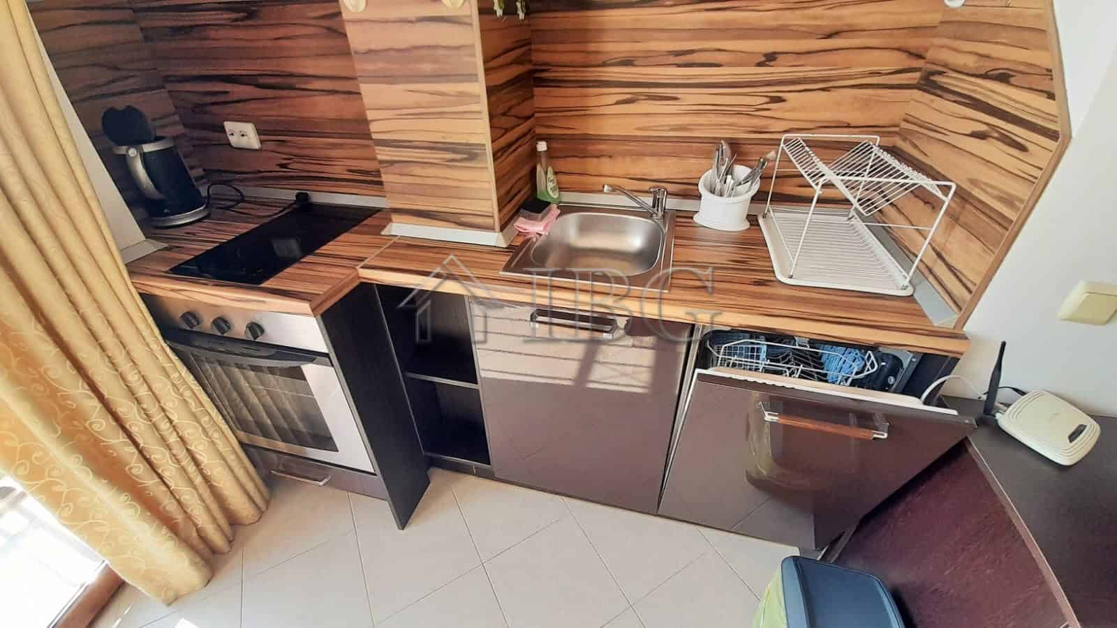 Kitchen with balcony access, featuring wooden cabinets, sink, stove, and compact appliances.
