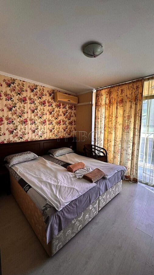 Comfortable bedroom with balcony, floral wallpaper, and partial sea view in Sunny Beach.