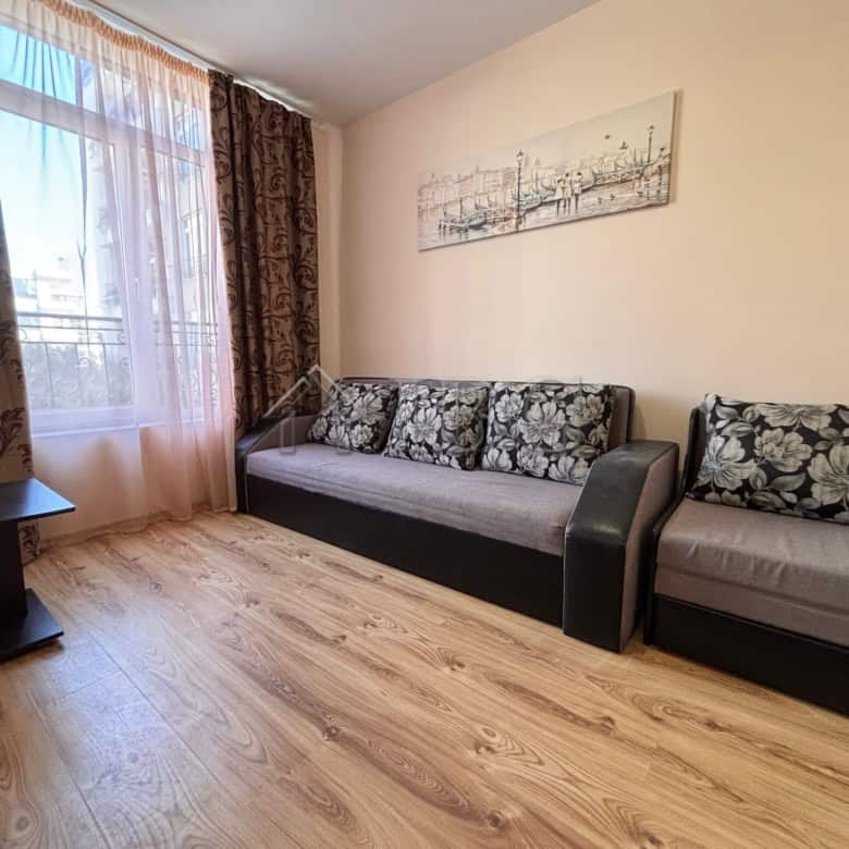 Spacious living room with sofa and armchair, large window with curtains, and artwork on the wall.