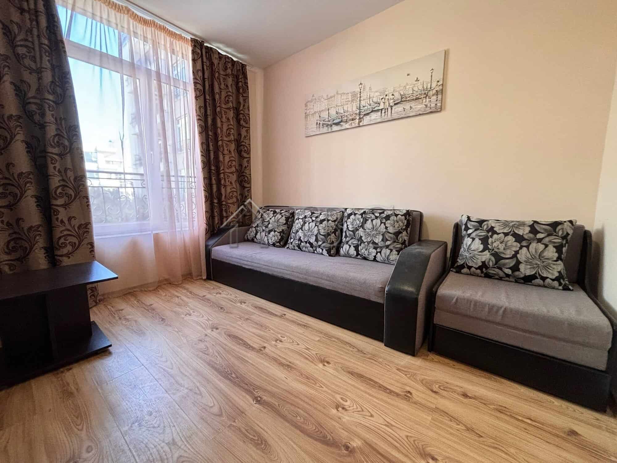 Spacious living room with sofa and armchair, large window with curtains, and artwork on the wall.