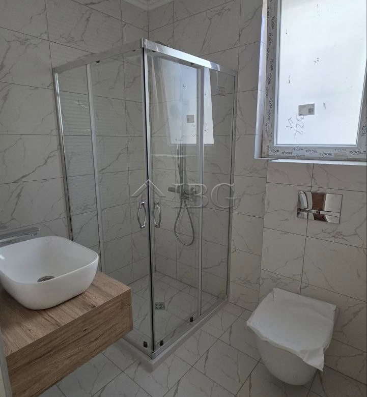 Modern bathroom featuring a glass shower enclosure, a wall-mounted toilet, and a window for natural.