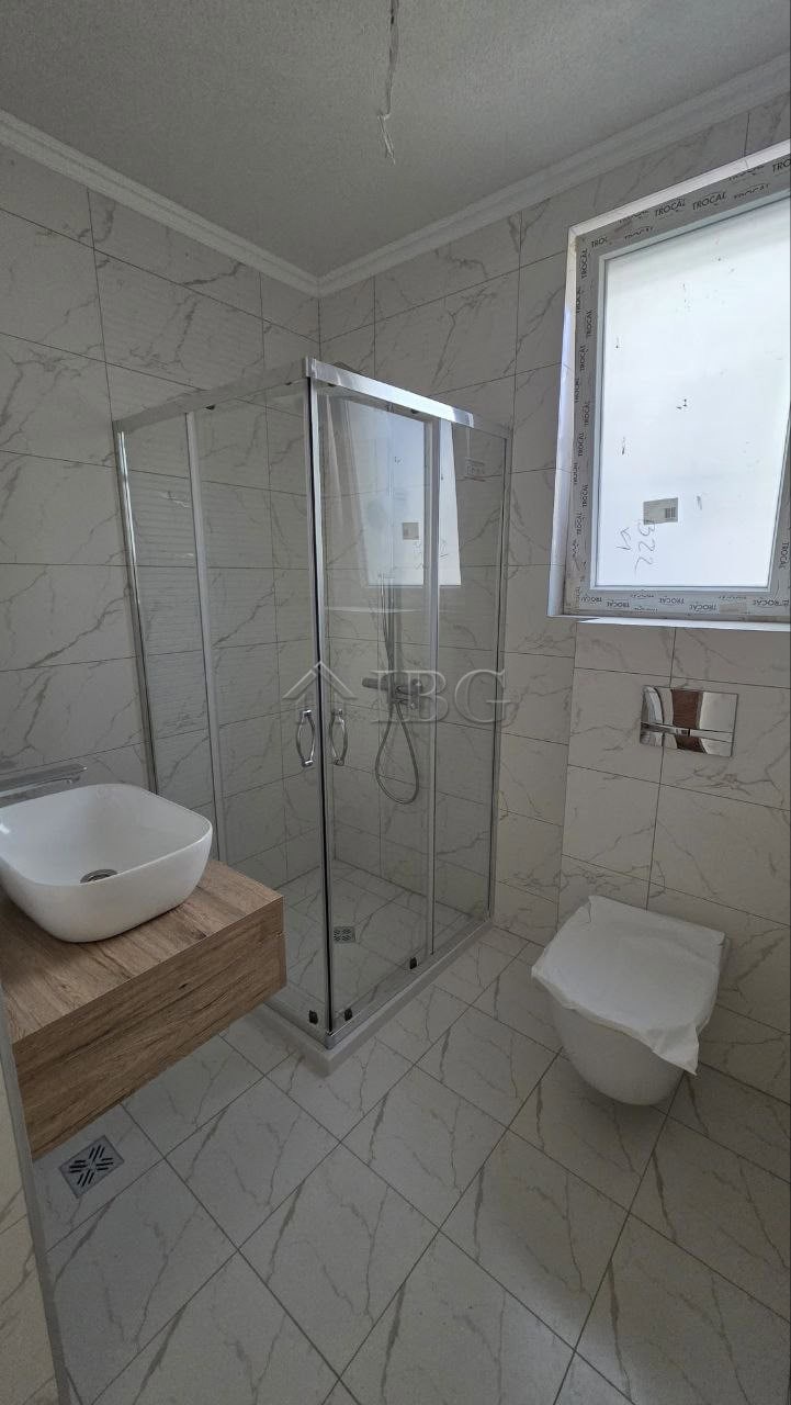 Modern bathroom featuring a glass shower enclosure, a wall-mounted toilet, and a window for natural.