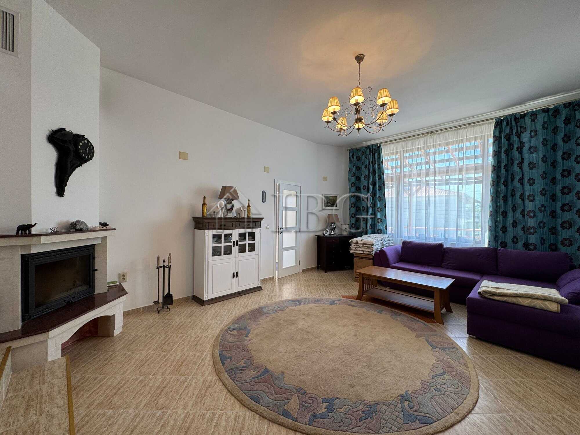Bright living room with large window, purple sofa, and elegant chandelier in Kosharitsa home.