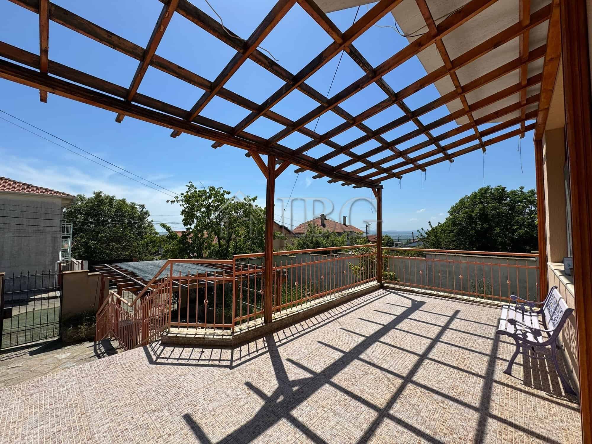 Large outdoor balcony with wooden pergola overlooking lush greenery and distant sea views. Perfect f.