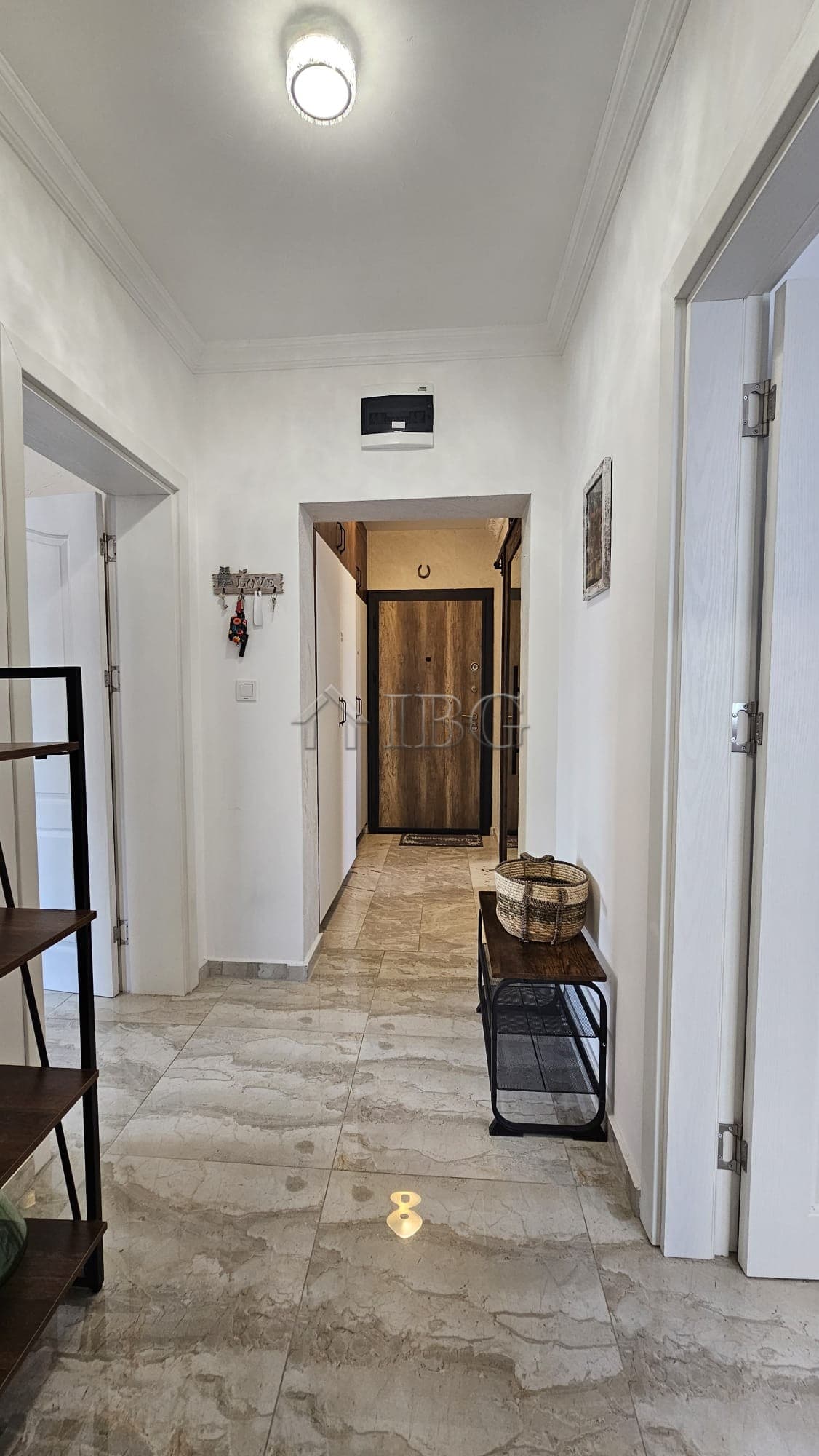 Interior view of a bright, spacious apartment hallway with white walls and marble flooring.