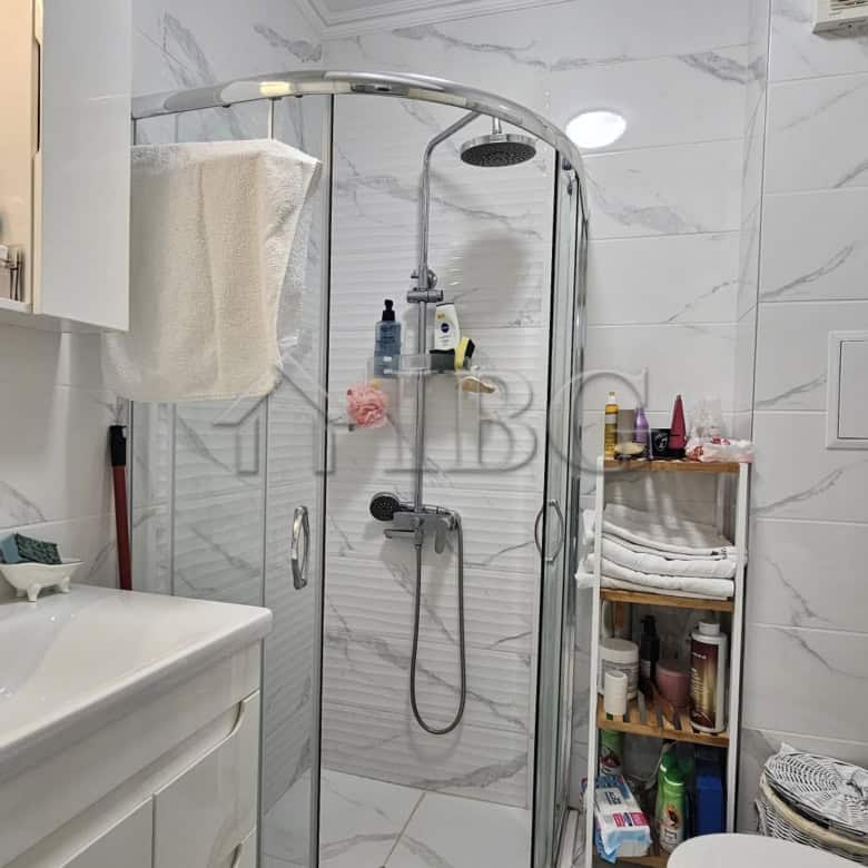 Bathroom with shower, sink, and storage shelves in a contemporary apartment.