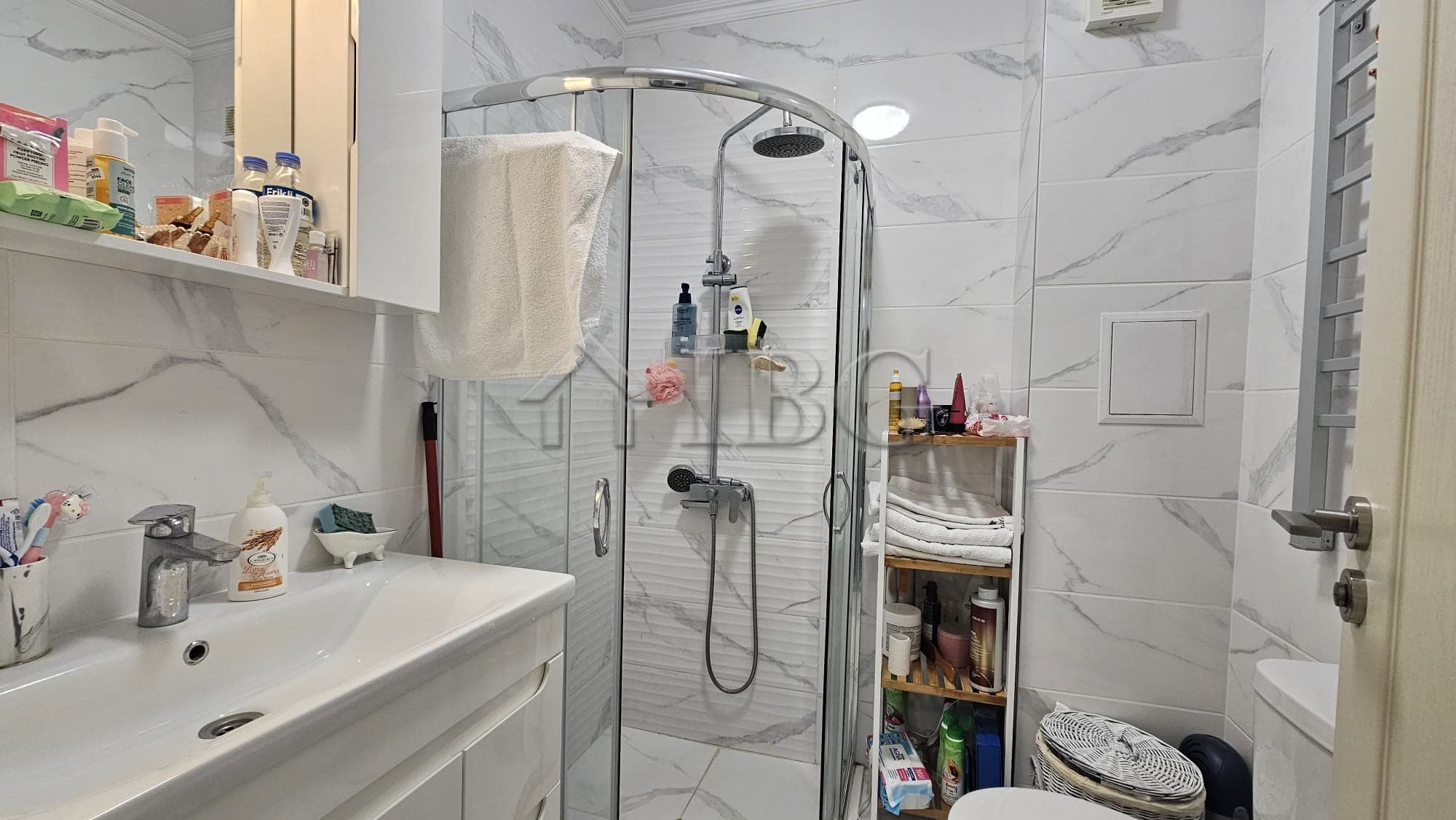 Bathroom with shower, sink, and storage shelves in a contemporary apartment.
