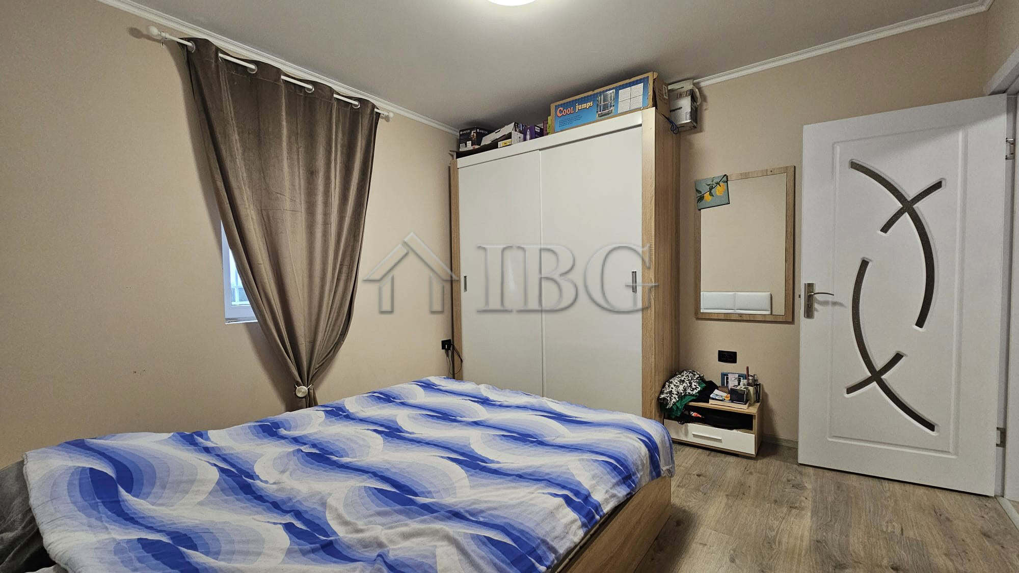 Interior view of a bedroom with a bed, wardrobe, and window with curtains.