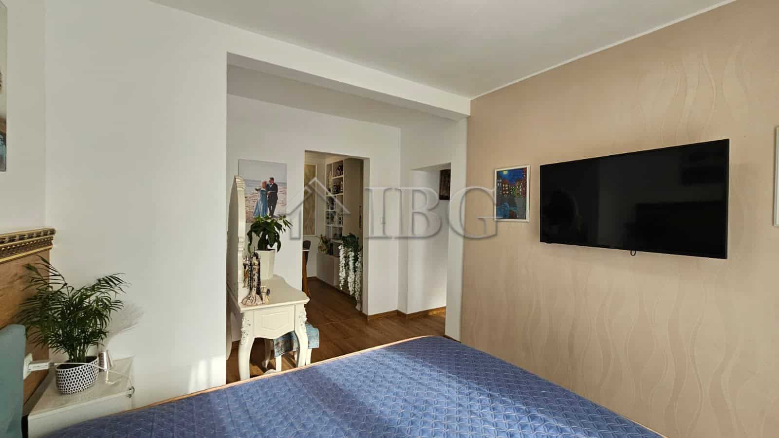 Modern bedroom with blue bedspread, wall-mounted TV, and stylish decor in Kosharitsa.