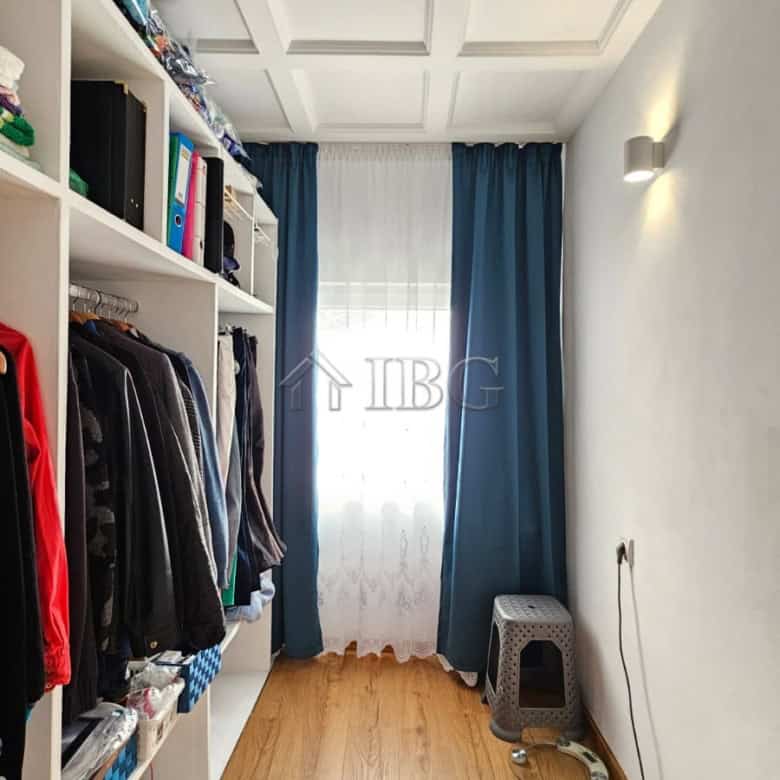 Spacious walk-in closet featuring a wardrobe, window with blue curtains, and wooden flooring in a re.