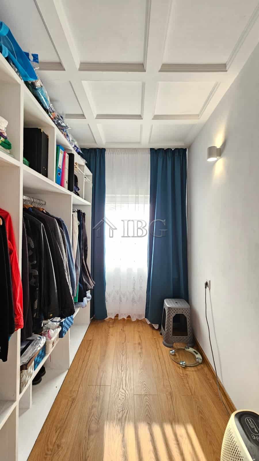 Spacious walk-in closet featuring a wardrobe, window with blue curtains, and wooden flooring in a re.