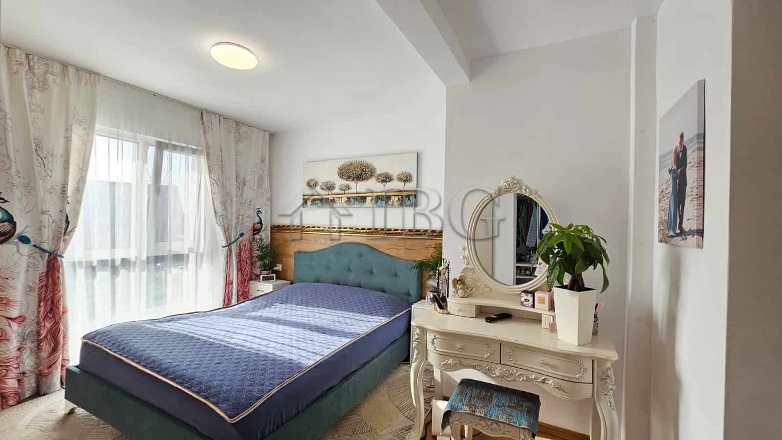 Bright bedroom with large window, blue bed, and elegant white furniture in renovated house.