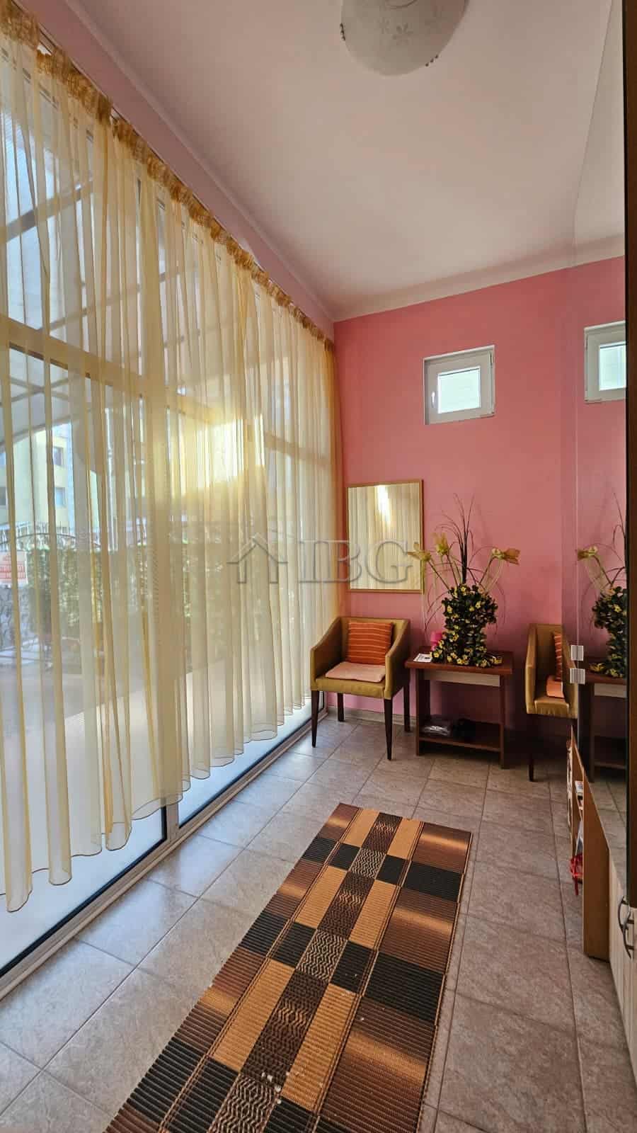 Sunlit interior with pink walls, large windows with sheer curtains, and cozy seating area in a comme.