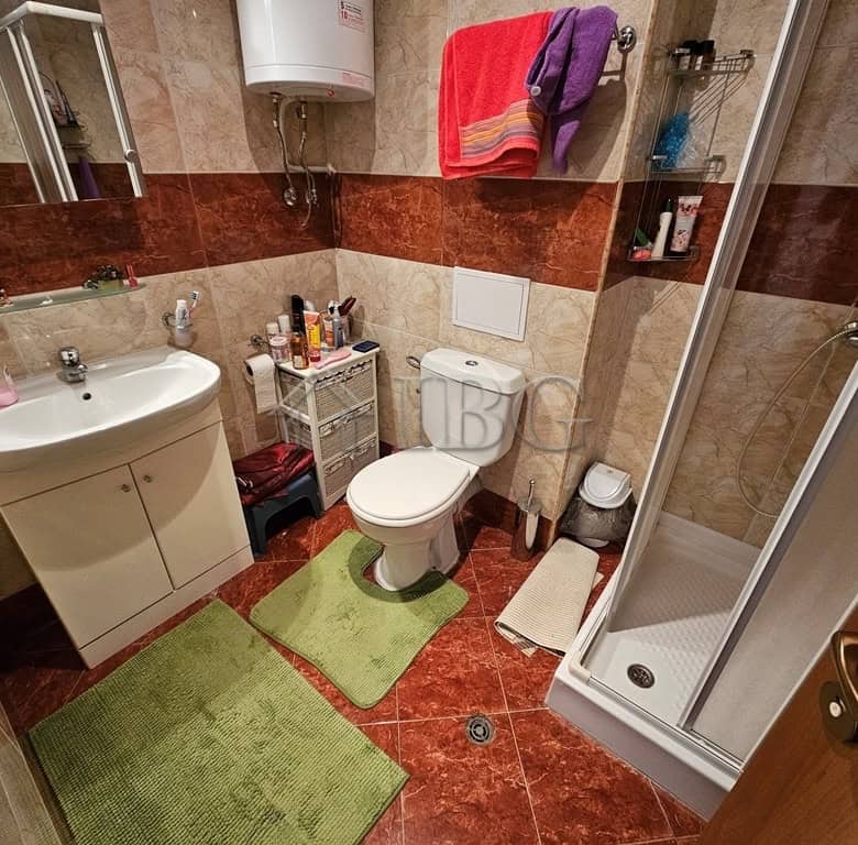 Bright bathroom featuring a white sink, toilet, and shower cabin with beige and brown tiled walls.