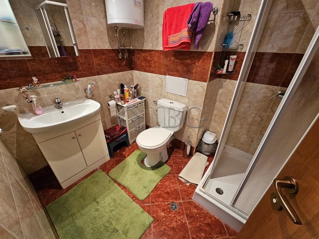 Bright bathroom featuring a white sink, toilet, and shower cabin with beige and brown tiled walls.