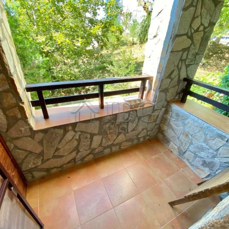 Bright balcony with stone walls and lush greenery view.