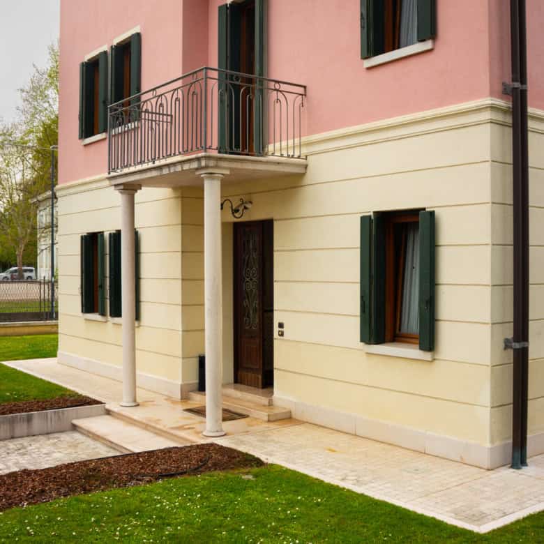 Elegant pink and cream villa with a small balcony and green shutters.