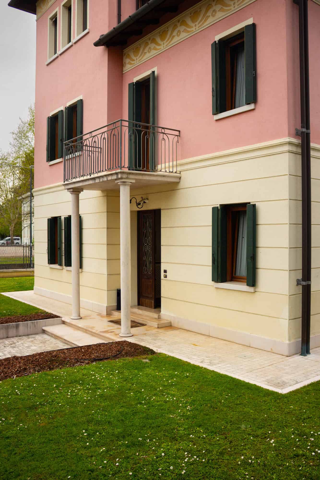 Elegant pink and cream villa with a small balcony and green shutters.
