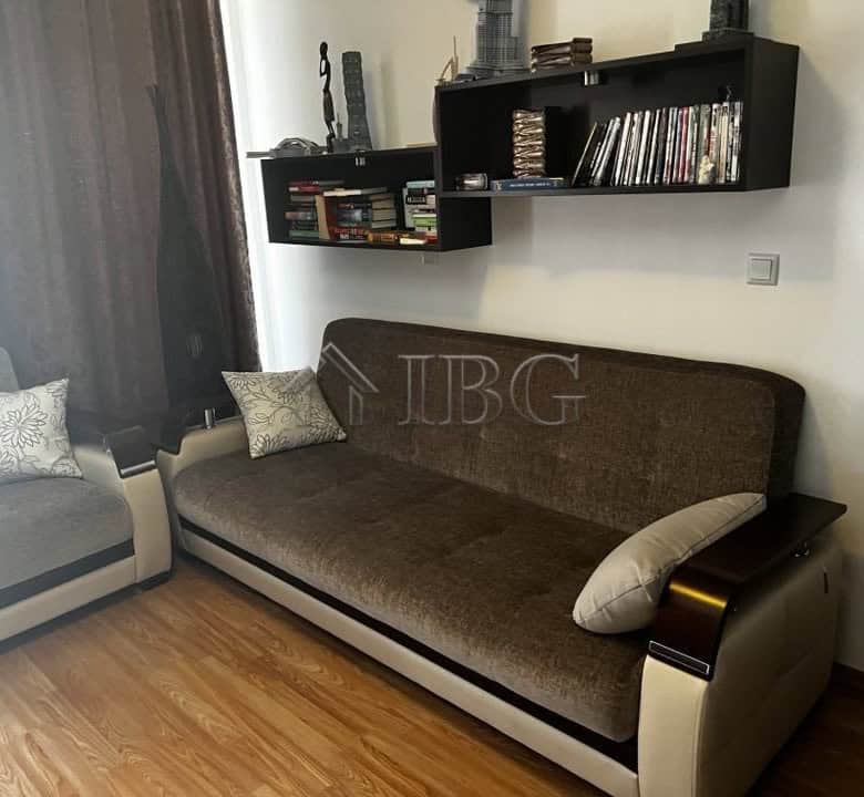 Bright living room featuring a brown sofa, armchair, and wall-mounted shelves with books and decor.
