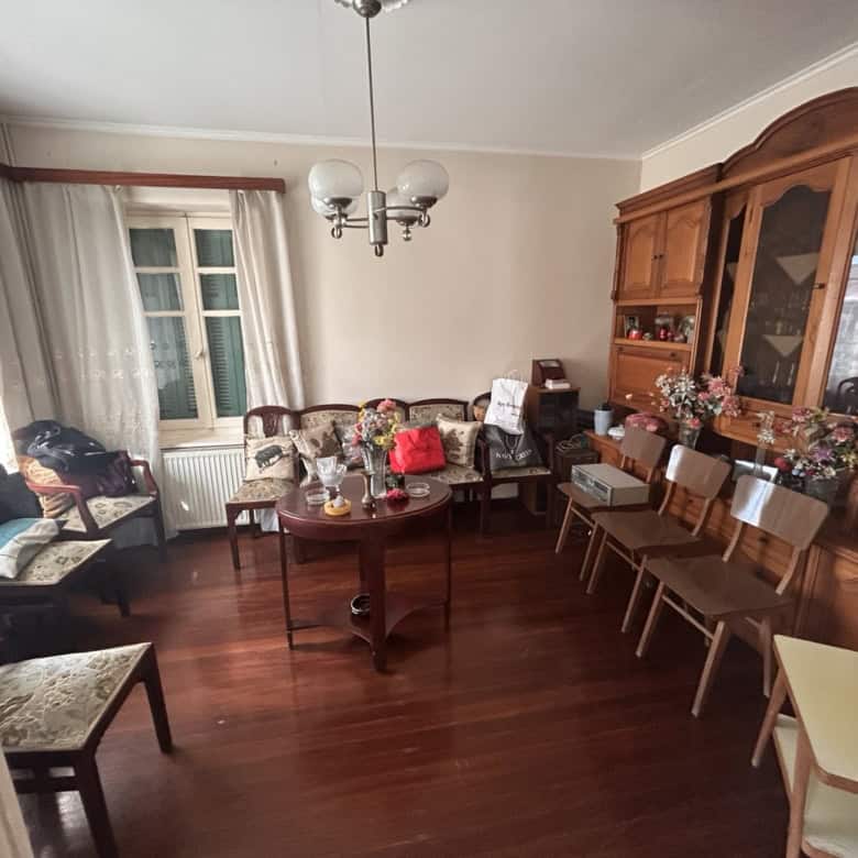 Spacious living room featuring vintage wooden furniture, a chandelier, and large windows with curtai.