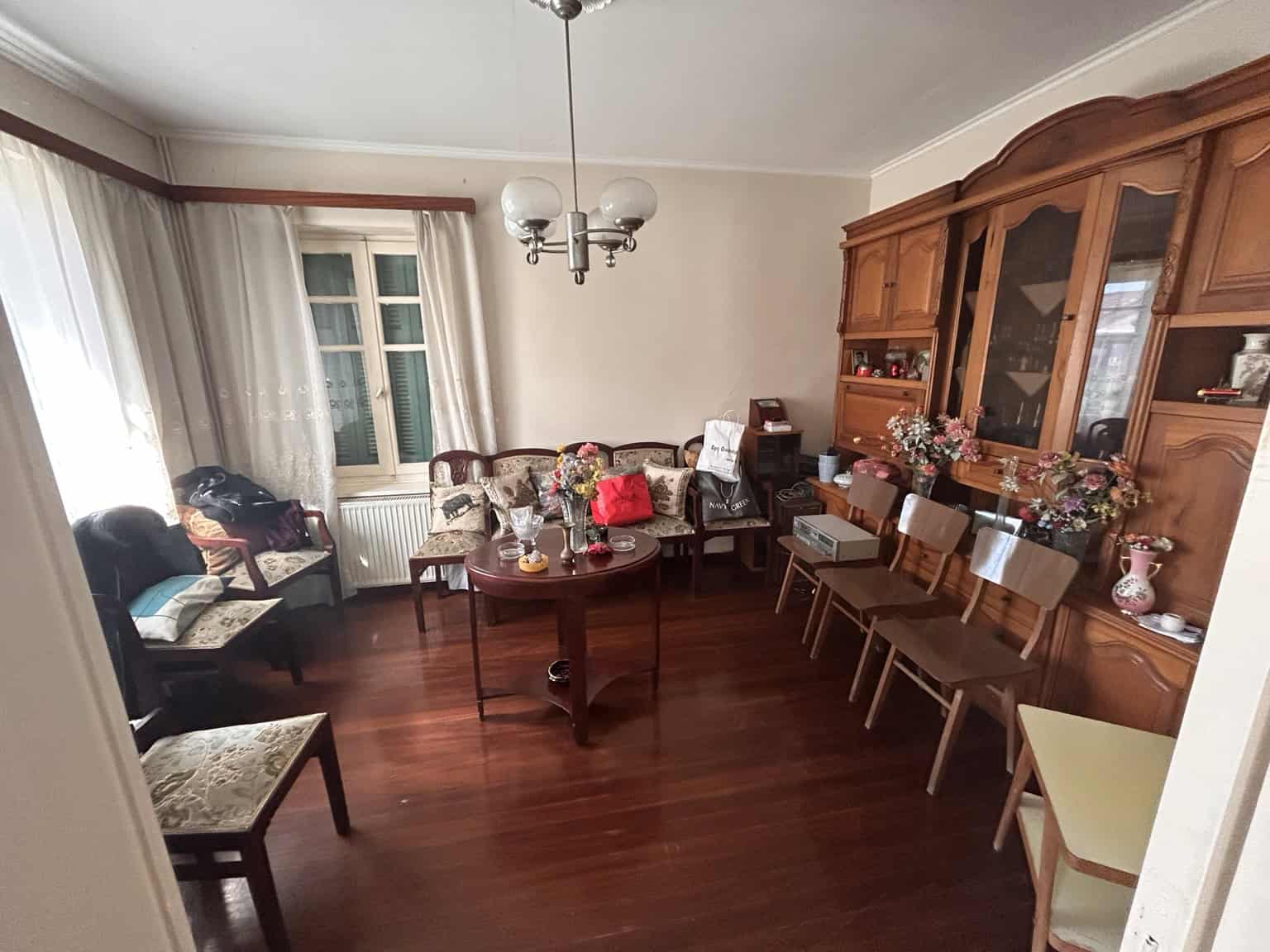 Spacious living room featuring vintage wooden furniture, a chandelier, and large windows with curtai.