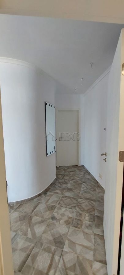 Interior view of a bright, minimalist apartment corridor with white walls and tiled flooring.