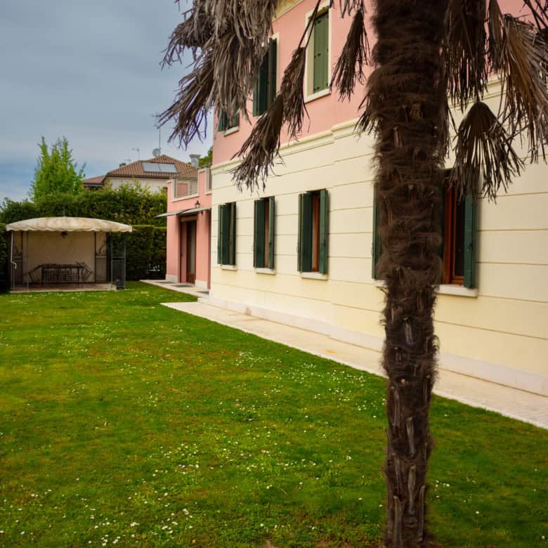 Elegant Mediterranean villa with lush garden and tall palm tree in a sunny setting.