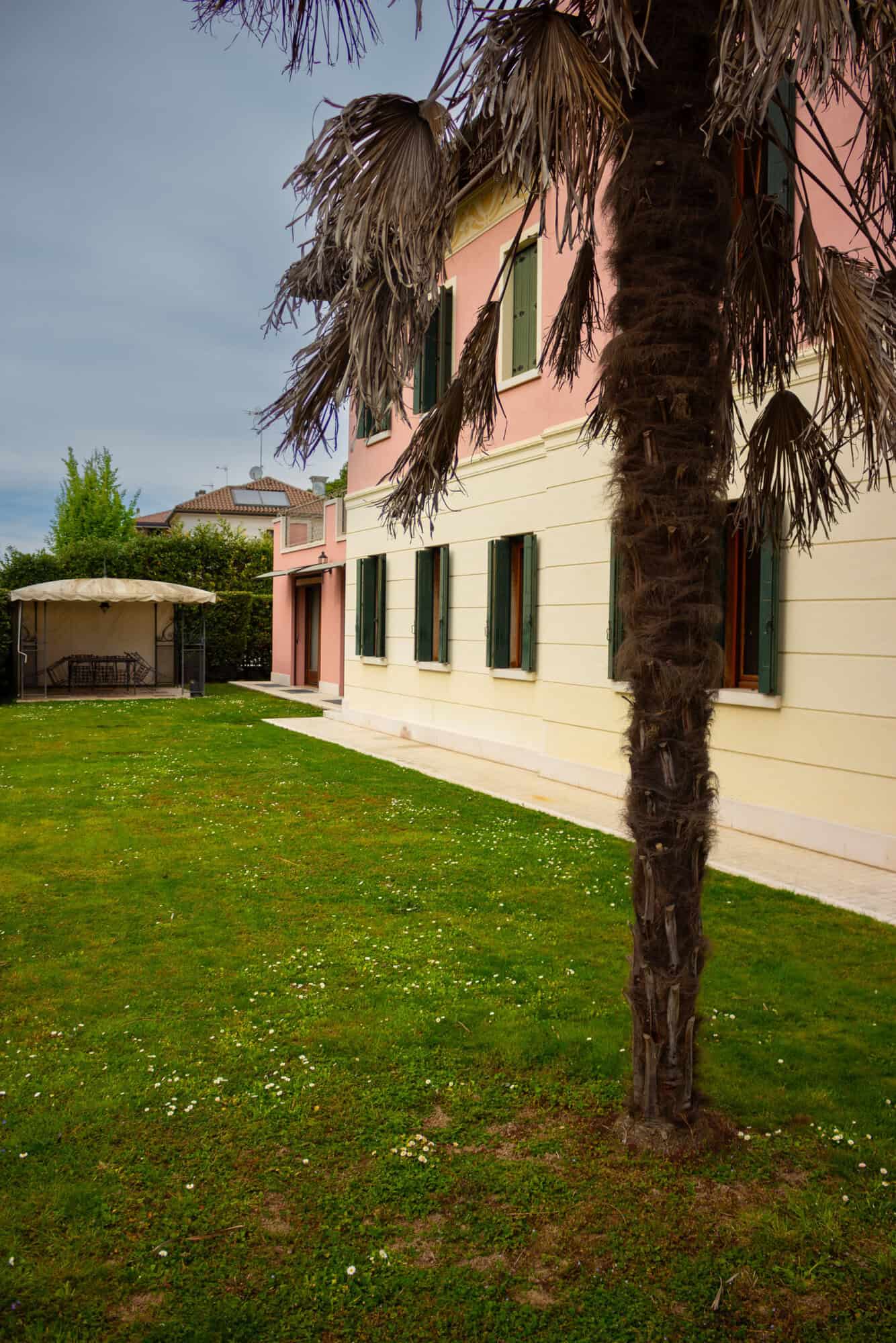Elegant Mediterranean villa with lush garden and tall palm tree in a sunny setting.