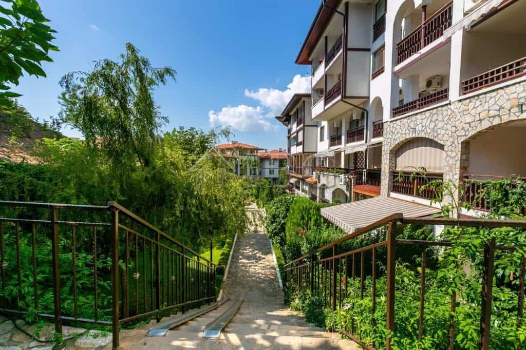 Apartment with balconies overlooking lush garden and pathway.