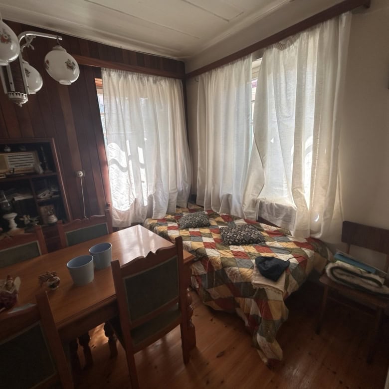 Spacious room with large windows, curtains, and a cozy bed with a colorful quilt.