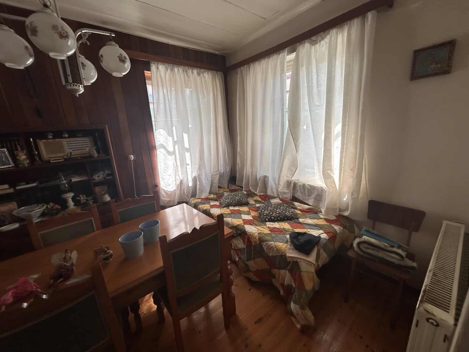 Spacious room with large windows, curtains, and a cozy bed with a colorful quilt.