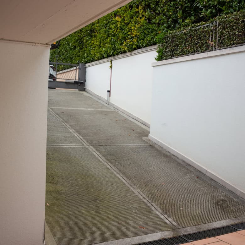 Underground parking ramp with white walls, sloped driveway, and greenery in the background.