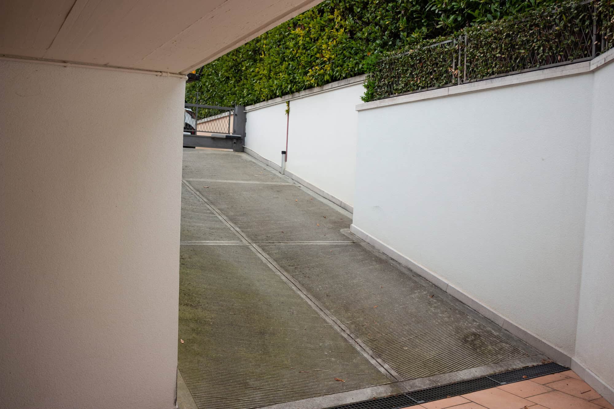 Underground parking ramp with white walls, sloped driveway, and greenery in the background.