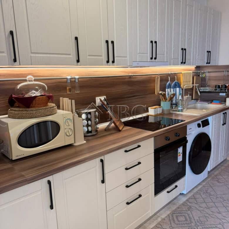 Bright kitchen featuring white cabinetry, black handles, and essential appliances.
