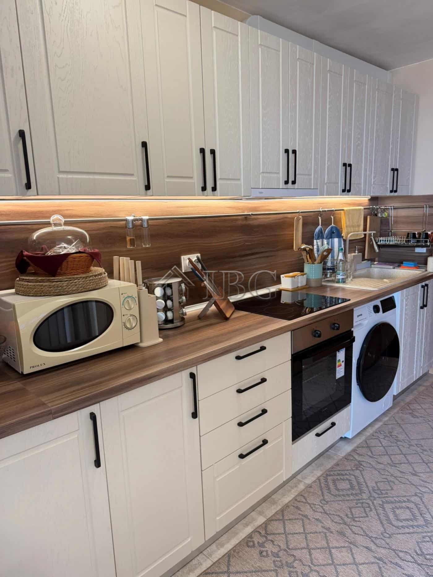 Bright kitchen featuring white cabinetry, black handles, and essential appliances.