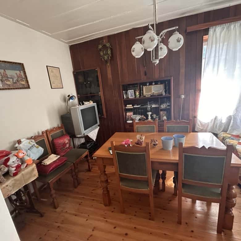 Bright living room with wooden furniture, dining table, and sunlight streaming through curtains.